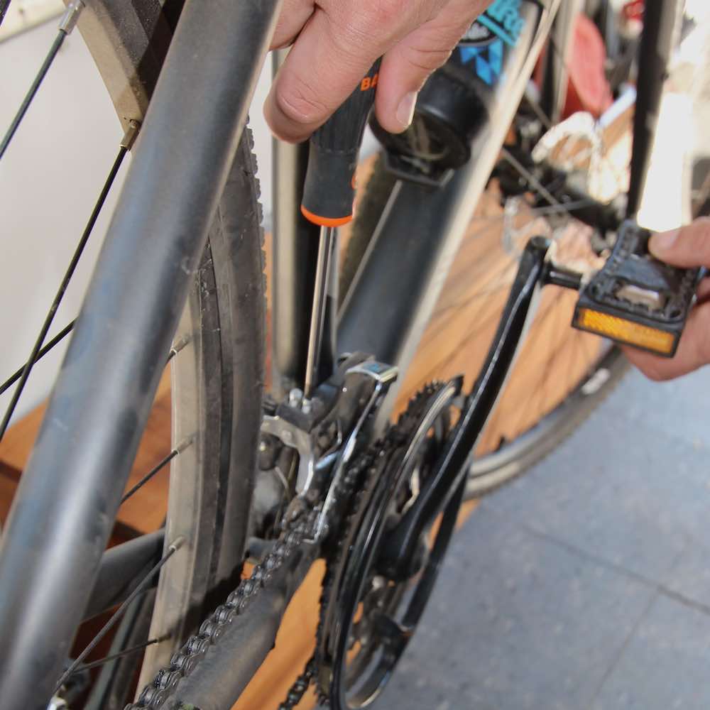mecanico de bicicleta regula (sincroniza) desviador o descarrilador de cambios durante mantencion a bordo de taller movil chum